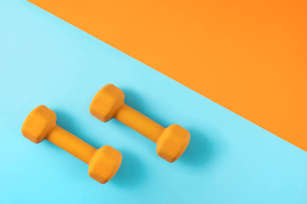 istock Dumbbells on Orange and Blue Background 1253261565