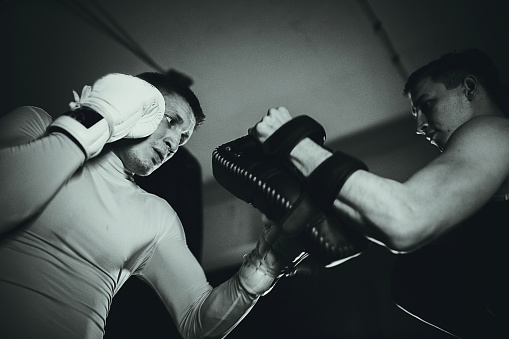 Two young men, kick boxer and his coach, sparring together in the gym.