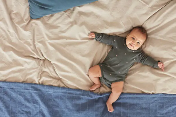 Top down view at cute mixed-race baby lying on comfortable bed with fluffy blue and white blankets, copy space
