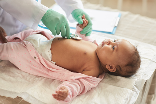 Close up of unrecognizable doctor examining cute mixed-race baby lying on changing table in clinic, copy space