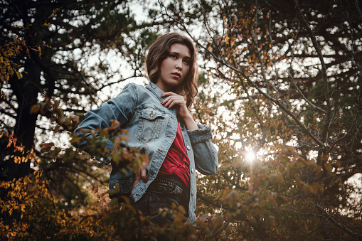 Beautiful Asian woman in a golden autumn forest. Solitude or depression concept. Millenial dealing with problems and emotions.