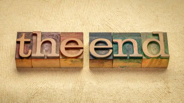 The end concept - words in vintage wooden letterpress printing blocks stained by color inks against handmade textured paper