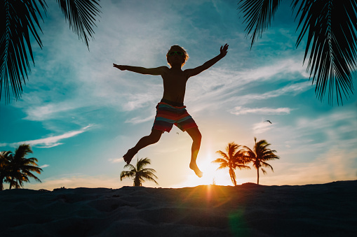 happy boy enjoy sunset on tropical beach with palm trees, vacation joy