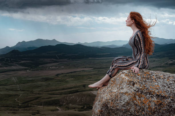istock Ginger woman sits on a cliff and looks at an impending storm 1253269457
