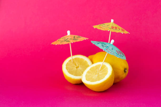 istock Lemon with colorful cocktail umbrellas under intense light on pink background 1253270904