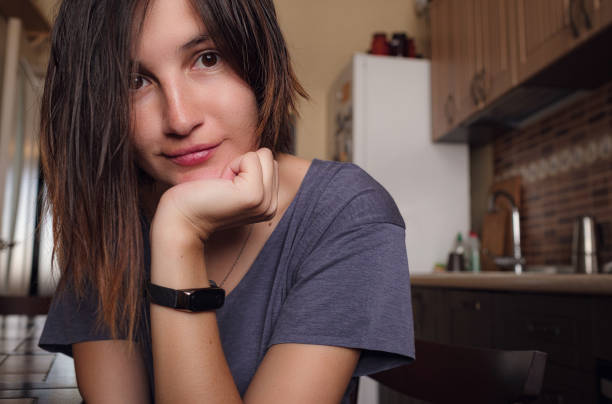 Young woman sits by the table in the kitchen. Self care,staying home. Quarantined person indoors. Serene mornings. Avoiding social contact.