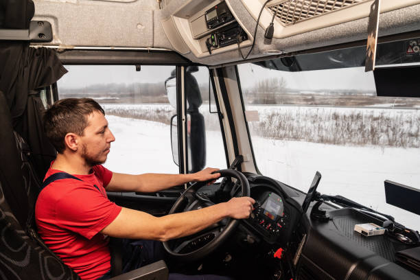 conducteur dans un t-shirt rouge au lieu de travail au volant d’un camion. vue intérieure de la cabine - semi truck truck red truck driver photos et images de collection