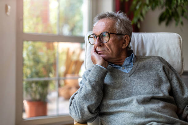 homme aîné regardant par la fenêtre à la maison - vieux photos et images de collection