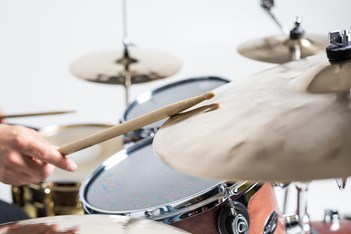 Close up of hands of male drummer holdning drumsticks sitting and playing drums in studio