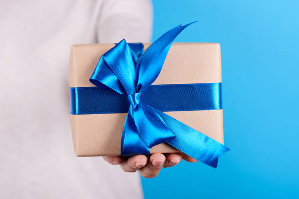 istock Present box with blue ribbon in hand. 1253278635