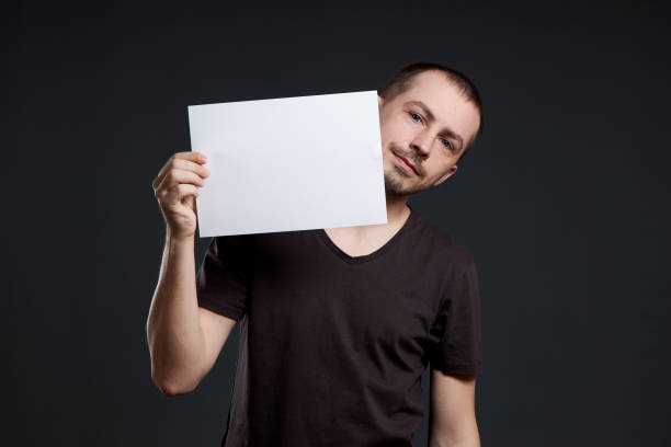istock Man holds an empty poster paper sheet in his hands. Smile and joy, place for text, copy space 1253281248