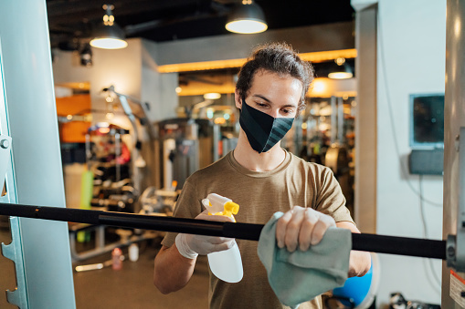 A gym owner is cleaning and disinfecting sports equipment in the gym for reopening.