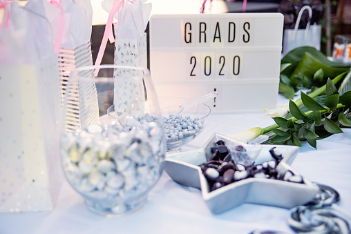 Celebrating graduation in the backyard element of decoration during Covid-19 pandemic. Close-up on sign with « Grads 2020 » written on it. Outfocus candy bowls in the foreground. Horizontal outdoors shot with copy space.