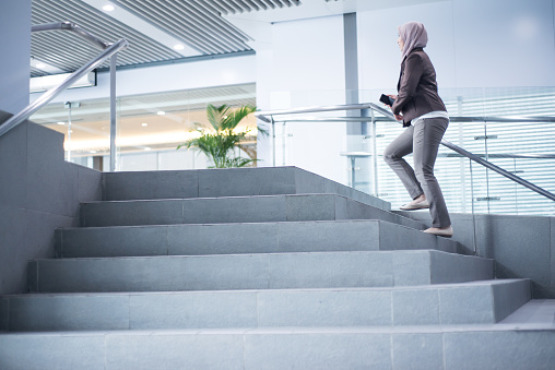 Asian Muslim Businesswoman walking up the stairs in modern city in rush hour to work