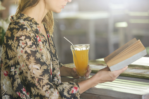 Relaxed young woman having a orange juice and reading a book