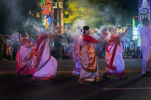 Kolkata, West Bengal, India - 3rd October 2017 : Bengali Hindu ladies dressed in red and white Saris, traditional Indian dress, are dancing with holy smoke at Durga Puja carnival on Red Road at night.