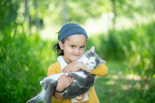 A cute little girl snuggles with her cat outside.