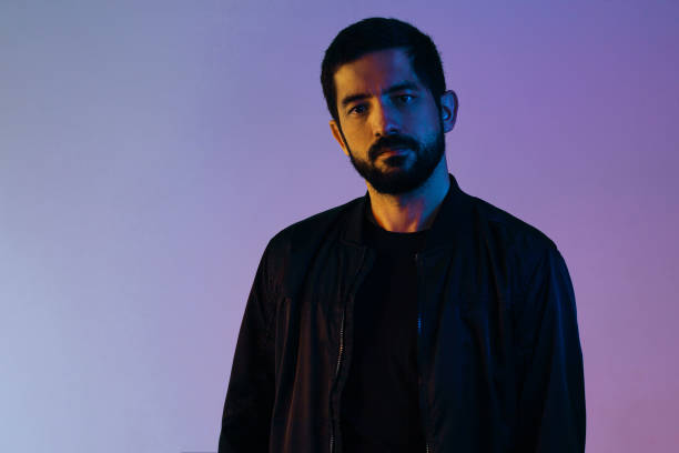 istock Dramatic portrait of man wearing jacket lit by blue and red lights. 1253291814