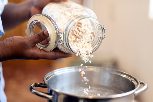 Close up woman pours dried beans and maize into cooking pot