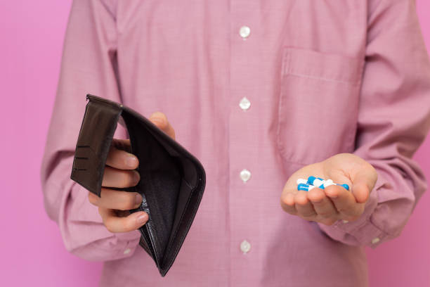 istock The guy shows an empty wallet and pills. Expensive pills. A crisis. Pink background 1253306622