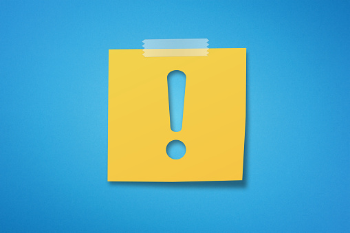 Yellow sticky note paper with exclamation mark on blue background