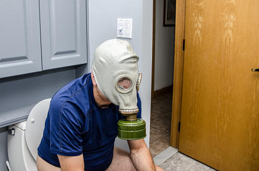 Hombre adulto sentado en el inodoro con máscara de gas photo