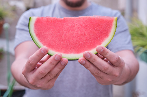 Unrecognizable man offering a seedless watermelon slice. Fruit, summer concept.