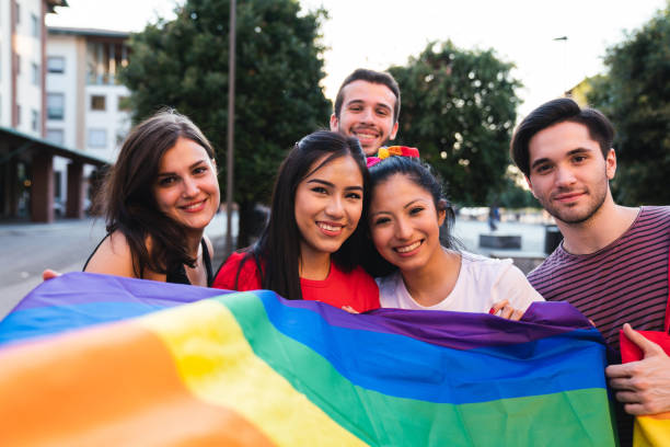 Five friends together at an LGBTQI Pride event Five friends together at an LGBTQI Pride event. Hispanic and caucasian ethnicities. They are looking at camera and smiling. rainbow flag photos stock pictures, royalty-free photos & images