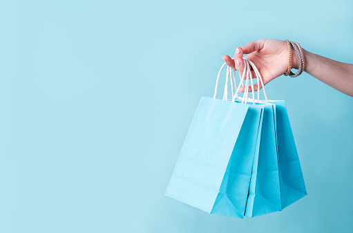 woman hand carrying a bunch of blue shopping bags over blue background with copy space