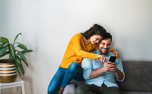 Man holding in hands cell phone and woman showing screen and smiling together at home