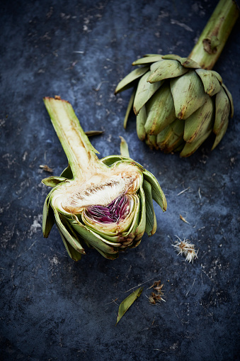 A cut open artichoke and a whole one on a blue stone underground.