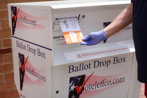Gloved hand inserting ballot into ballot box in Jefferson County Colorado primary election in early voting in June 2020