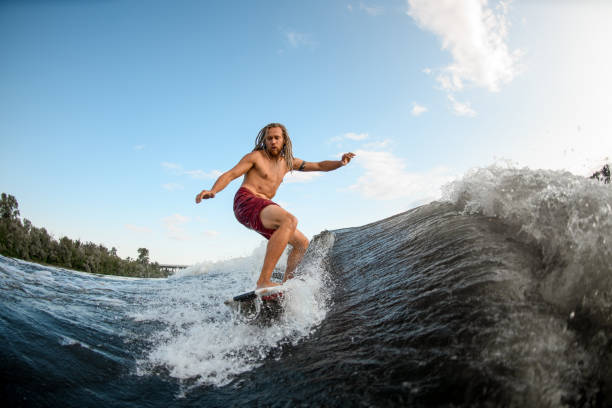 istock young man wakesurfer with dreadlocks ride the waves on surfboard. 1253324554