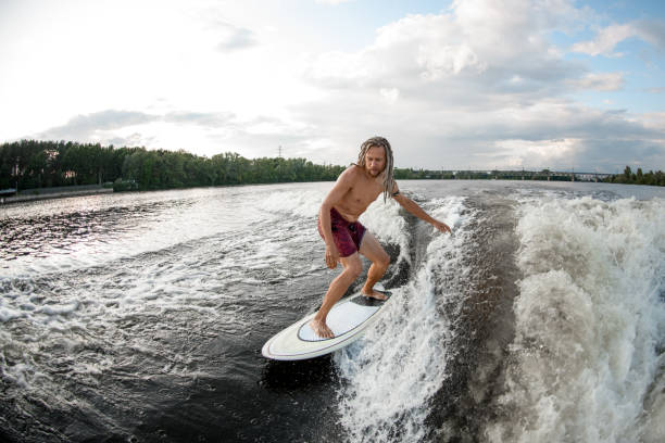 giovane sportivo wakesurfer con dreadlocks cavalcare le onde su tavola da surf. - wakeboarding surfing men vacations foto e immagini stock