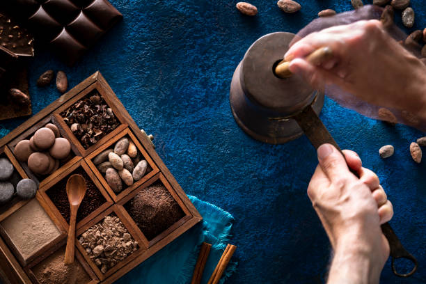 Chocolate pot copper grinding cocoa with hands holding stick with assorted chocolate box with drops cocoa powder and chocolate beans