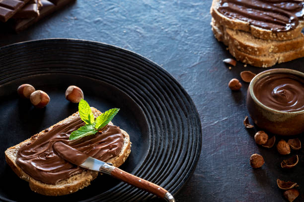 istock Chocolate cream spread on bread slice and hazelnuts on a dark black plate 1253325950