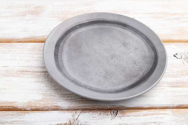 istock Empty gray ceramic plate on white wooden background. Side view, close up. 1253326571