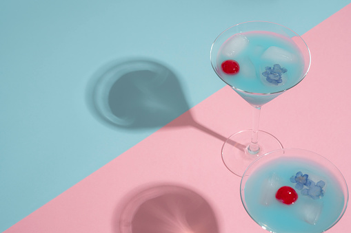 Blue Lagoon cocktail with cherry and purple flowers in ice cubes in pink and blue pastel background