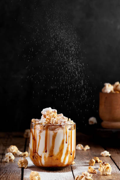 istock Milkshake with popcorn and caramel syrup on a black background. Sprinkle with powdered sugar. 1253328347