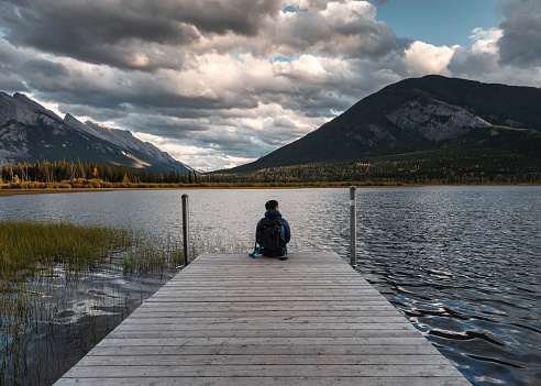 Man backpacker sitting on wooden pier in Vermillion lake at Banff national park, Canada