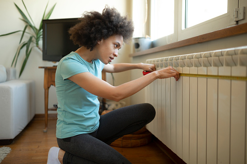 Young female African American interior designer using a measurement tape at home before proceeding with the DIY home improvement