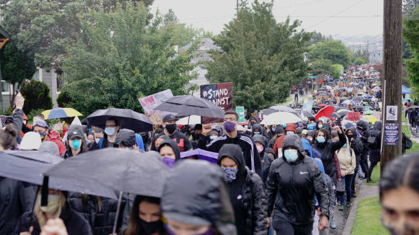 silent protesters march in the rain through neighborhoods in seattle calling attention to the black lives matter movement and police brutality - anti racism imagens e fotografias de stock