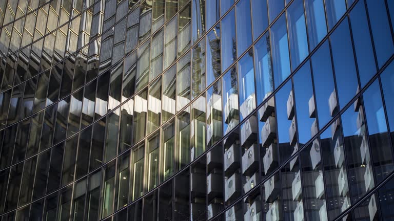 Time lapse shot of a curved glass building reflecting the surrounding buildings, moving clouds and changing sunlight.