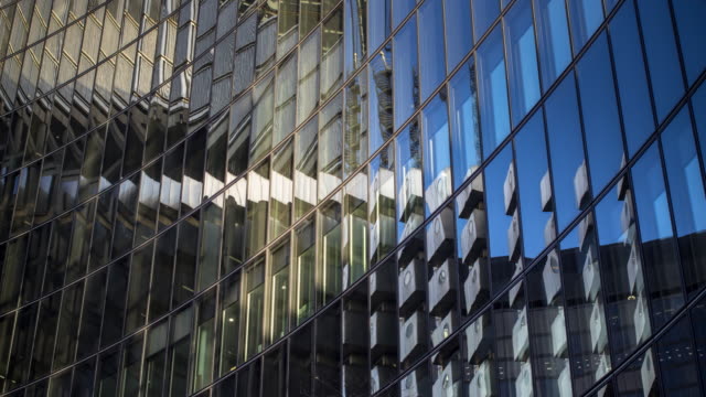 Time lapse shot of a curved glass building reflecting the surrounding buildings, moving clouds and changing sunlight.