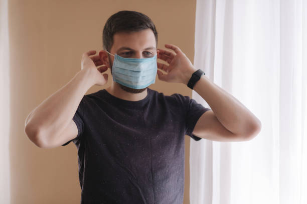 istock Man put on madical mask at home. Young man in protective mask. Coronavirus theme 1253341217