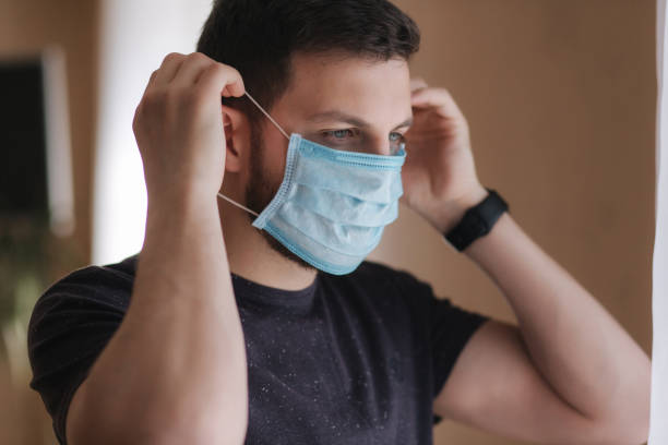 istock Man put on madical mask at home. Young man in protective mask. Coronavirus theme 1253341299