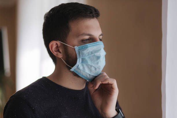 istock Man put on madical mask at home. Young man in protective mask. Coronavirus theme 1253341343