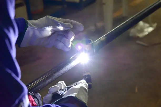 The welder is welding the pipeline with Tungsten Inert Gas Welding process (TIG). The welder wears protective equipment with a mask and heat resistant gloves