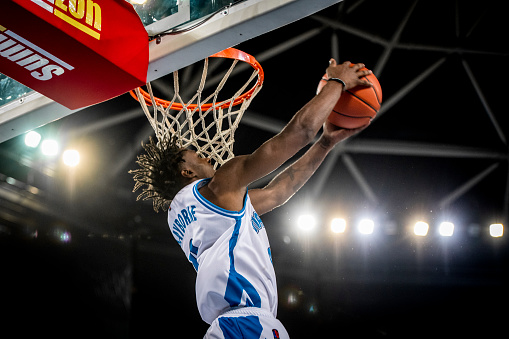 Low angle view of basketball player in white jersey slam dunking ball during the match.