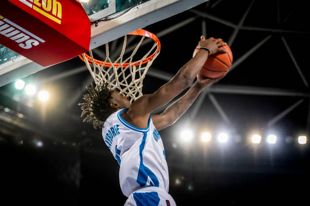 Basketball player slam dunking ball Low angle view of basketball player in white jersey slam dunking ball during the match. slam dunk stock pictures, royalty-free photos & images